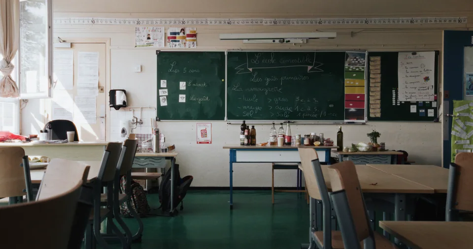 School classroom with desks, chalkboard, and chairs.