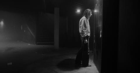 A woman stands in a dark room looking confused.