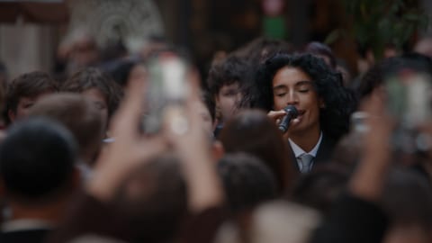 A group of people taking pictures and filming a singer performing in front of them.