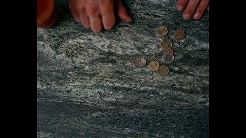 Picture of coins on rock with hands in top left corner